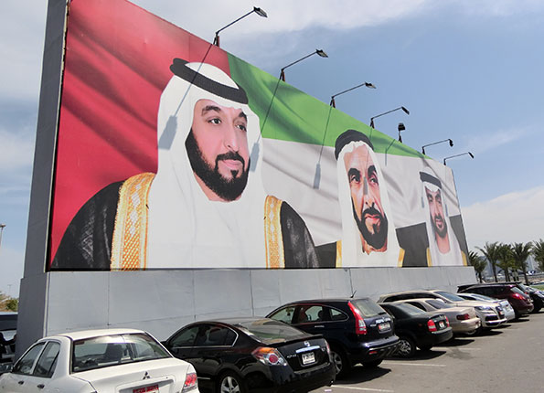 駐車場にある、UAE国旗を背景にする中東衣装の男性3人の看板