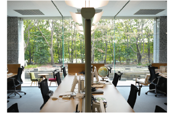 日中は自然光がふんだんに入り、豊かな緑も目に入る一面ガラス張りのオフィス